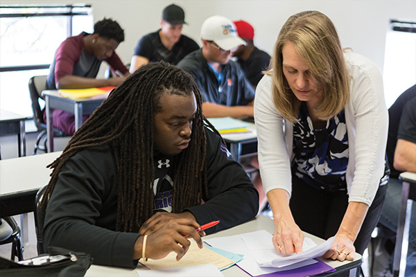 Female teacher explaining an assignment to male student with other male students in background