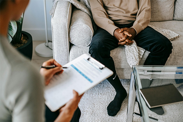 Close up of doctor holding a clipboard with a patient sitting on a couch