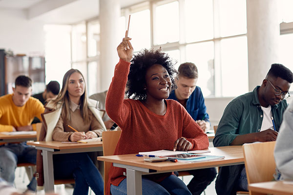 Smiling college student raises her hand in a full classroom