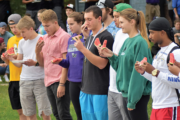 Group of diverse students standing in line eating watermellon