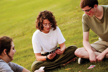 Two female and one male students playing UNO in the grass