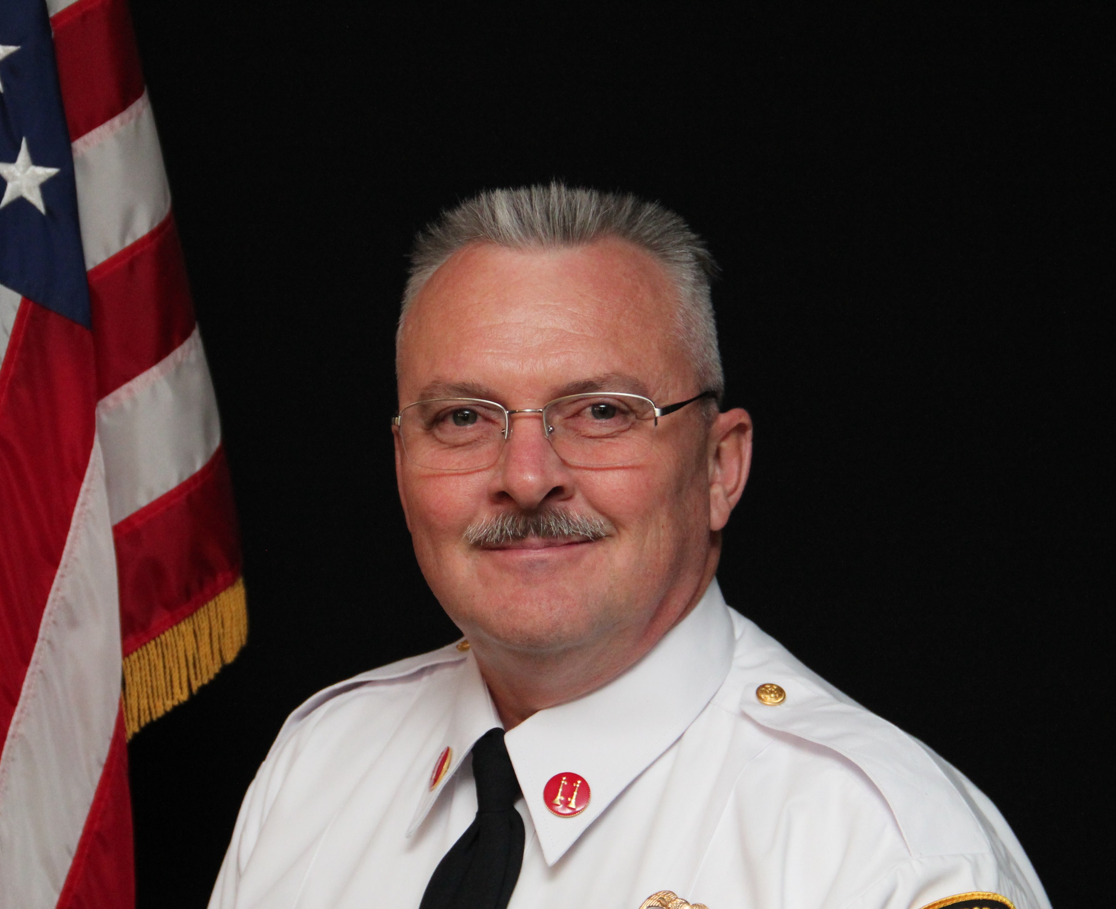 David Weber is wearing a black suit with a white shirt and red and blue striped tie.