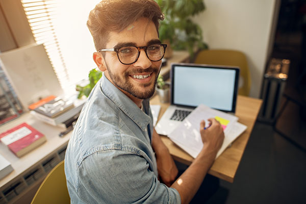 Student taking notes from a laptop turns to smile at camera